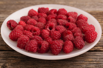 A plate full of raspberry on a wooden background