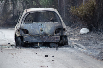 Obraz na płótnie Canvas After fire in Greece Burned car on road. Burnt tire and molten metal.Blurry people background