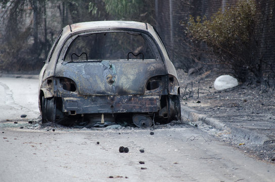 After fire in Greece Burned car on road. Burnt tire and molten metal.Blurry people background
