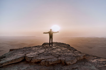 Alone man in israel negev desert admires the view of sunrise. Young male person stands on the edge of the cliff - obrazy, fototapety, plakaty