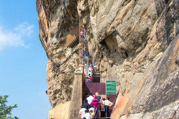 People climb up stairs and spiral stairs that leads to the cave with the famous frescoes of Sigiriya