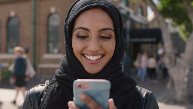 portrait of young pretty muslim woman watching video on smartphone laughing cheerful