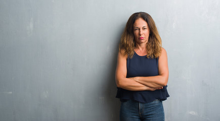 Middle age hispanic woman standing over grey grunge wall skeptic and nervous, disapproving expression on face with crossed arms. Negative person.
