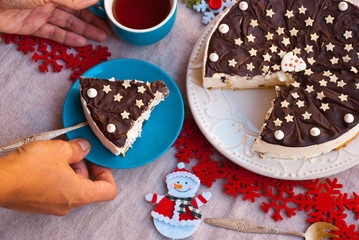 Woman hand with piece of christmas chocolate cake with holiday decoration and cup of tea.Food xmas background. Breakfast time.