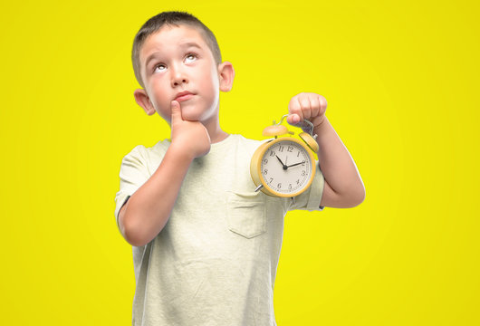 Little child holding alarm clock serious face thinking about question, very confused idea