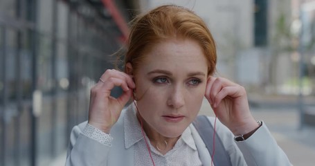 portrait beautiful young red head business woman intern puts on earphones listening to music in city enjoying relaxed urban lifestyle slow motion