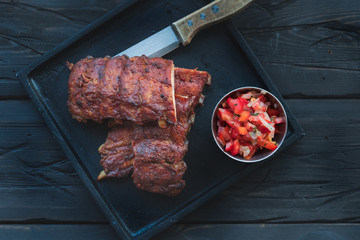 Schweine Spare Ribs aus dem Smoker  Barbecue Grill mit Salsa Dip und auf einem schwarzen Brett mit einem Mssser