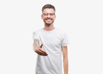 Young tattooed adult man smiling friendly offering handshake as greeting and welcoming. Successful business.