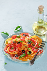 Veggie tomatoes summer salad with basil and olives on blue table.