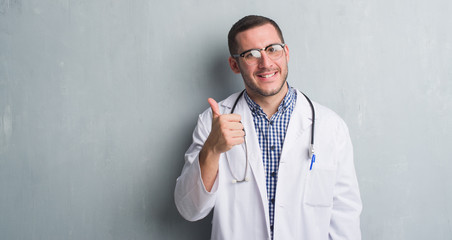 Young caucasian man over grey grunge wall wearing doctor uniform happy with big smile doing ok...