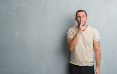 Obraz premium Young caucasian man over grey grunge wall asking to be quiet with finger on lips. Silence and secret concept.