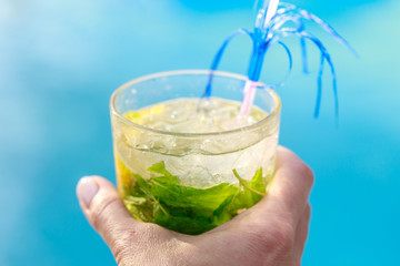 Large glass of cocktail with mint and lemon in hand on a blue background close-up