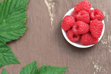 Large berries of ripe raspberries on the plate. Leaves and berries of raspberries close-up on a wooden background.