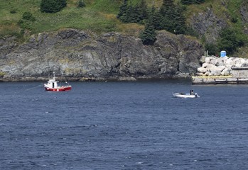 Obraz premium small red and white fishing boat anchored off shore near a rugged coastline