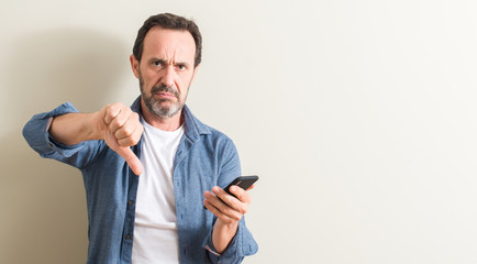 Senior man using smartphone with angry face, negative sign showing dislike with thumbs down, rejection concept