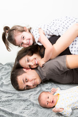 Happy family of four looking at the camera on their bed with child and newborn baby