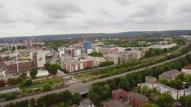 Drone panning left to right tracking train go through Hendon, North London UK town, during day time cloudy. Cranes and construction in background.