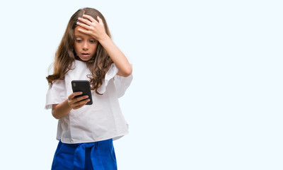 Brunette hispanic girl using smartphone stressed with hand on head, shocked with shame and surprise face, angry and frustrated. Fear and upset for mistake.