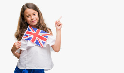 Brunette hispanic girl holding flag of United Kingdom very happy pointing with hand and finger to...