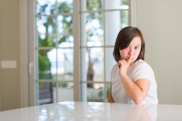 Down syndrome woman at home asking to be quiet with finger on lips. Silence and secret concept.