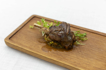 roasted meatshank baked whole lies with fresh tomato greens and hot pepper on a platter on an old wooden surface
