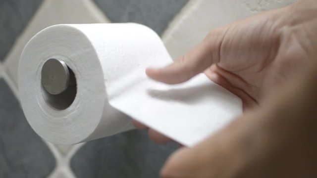 Hands cutting some toilet paper from the toilet paper roll.