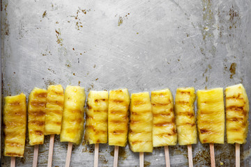 Flat lay of grilled pineapple on bamboo sticks  on tray. Copy space.