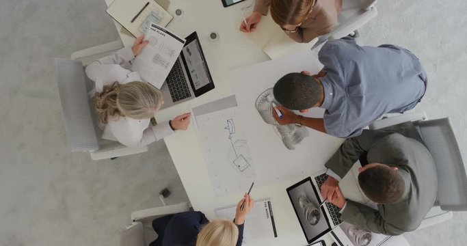 multi ethnic business people engineers planning ambitious turbine project brainstorming working on design schematics in corporate boardroom meeting top view