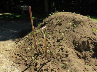A large pile of dirt and soil outside with shovels 