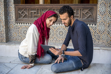 Young Muslim couple in relationship smiling while working on tablet