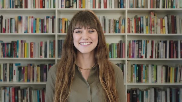 portrait of young pretty librarian woman smiling happy looking at camera in library bookshelf background