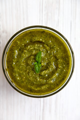 Bowl of freshly made basil pesto on white wooden table, top view. Closeup.