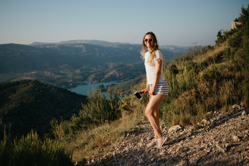 Fototapeta premium Cute girl dancing on the sandy road with canyon and emerald lake on the background on the sunset in Spain. Traveler in the mountains.