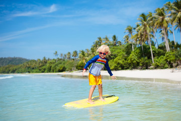 Child surfing on tropical beach. Surfer in ocean.