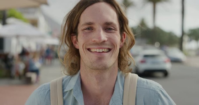 portrait of happy young caucasian man laughing enjoying independent vacation lifestyle handsome male tourist on sunny urban beachfront street slow motion