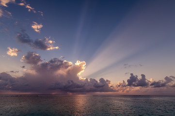 Sun rays behind tropical clouds over ocean at sunset