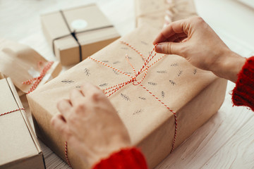 hands wrapping stylish christmas present with red ribbon. modern craft gifts on white wooden background. merry christmas concept.