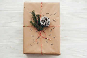 stylish christmas present with red ribbon, pine branches and cones. modern craft gift on white wooden background, flat lay. seasonal greetings card. merry christmas concept