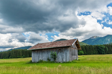 Fototapeta premium Idyllic landscape and a wooden mountain house in the Alps with green meadows and clouds