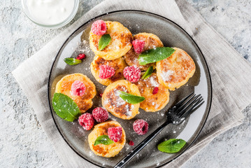 Healthy summer breakfast, cheese pancakes with raspberry, powdered sugar and mint, grey concrete background copy space