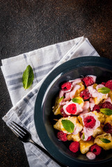 Ukrainian, Russian food, lazy vareniki; Curd or cheese gnocchi with fresh raw raspberries, cream and mint, on a dark concrete background, copy space top view
