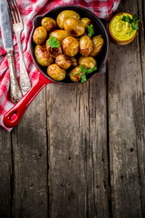 Baked in frying pan whole young potatoes, homemade vegetarian food, wooden old rustic table, with sauce, copy space above