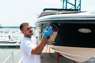 Boat maintenance - Man with orbital polisher polishing boat in marina.