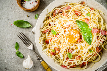 Traditional italian pasta, spaghetti carbonara with bacon, creamy sauce, parmesan cheese, egg yolk and fresh basil leaves grey stone background copy space