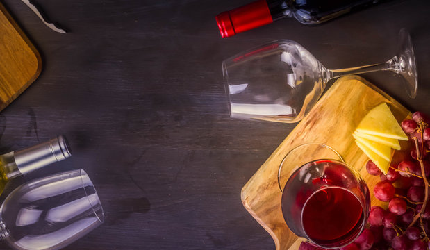 Bottle of red wine and two wine glasses on table with grape friut, copy space on dark table, toned image, banner