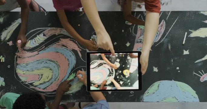 multi ethnic children drawing coloring space pictures together on blackboard using chalk happy kids enjoying fun creativity teacher taking photo using tablet top view