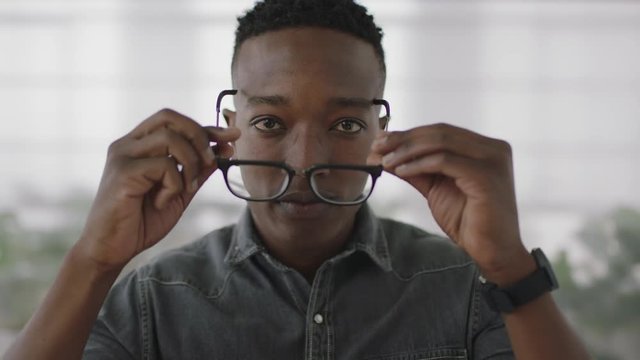 portrait of young male african american business student intern looking serious at camera puts on glasses smiling cheerful
