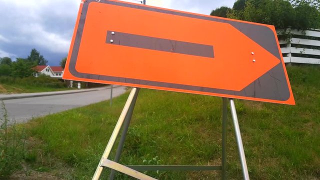 Camera moving down to show orange construction redirection sign, pointing right with street in the background