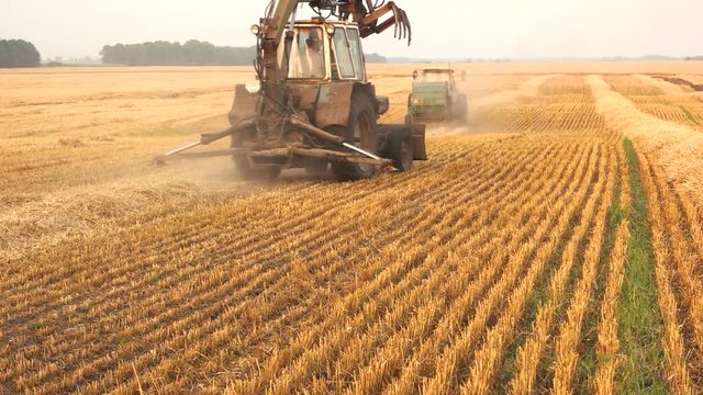 Tractor and harvester combiner on the field. Yellow stack of hay, agricultural tractors working on the farm.