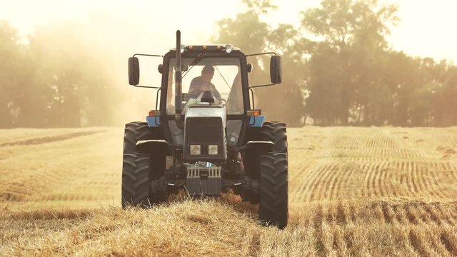 Tractor on the field, close up. Front view, driving tractor, yellow dry straw.